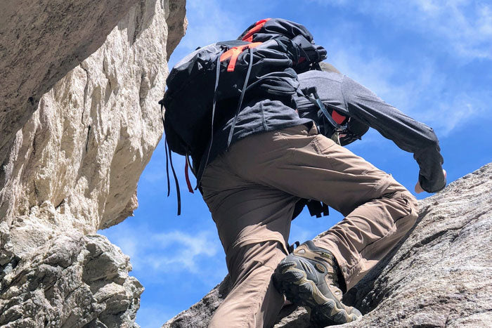 A hiker climbing a rocky mountain slope while wearing Moosehill 4-in-1 modular hiking pants for outdoor flexibility.
