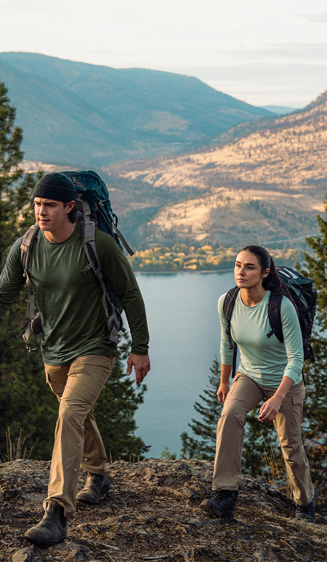 Moosehill HikerFlex series comfortable khaki men's and women's hiking pants worn by a couple trekking on a scenic mountain trail with a lake background.